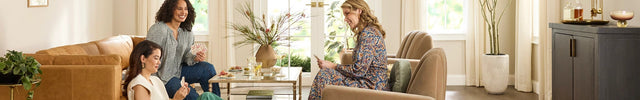 Three women sitting in a modern living room with large windows.