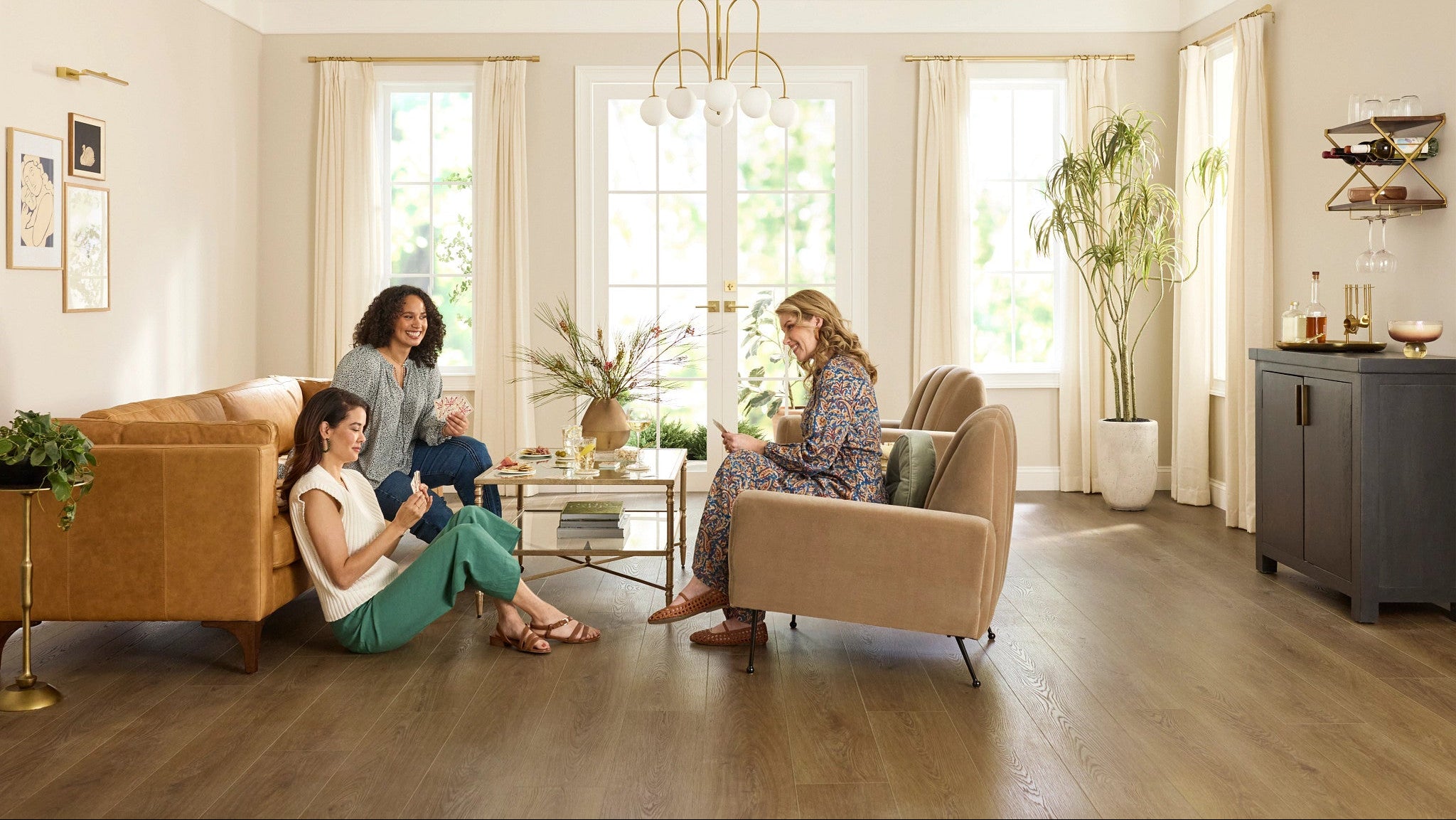 Three women sitting in a modern living room with large windows.