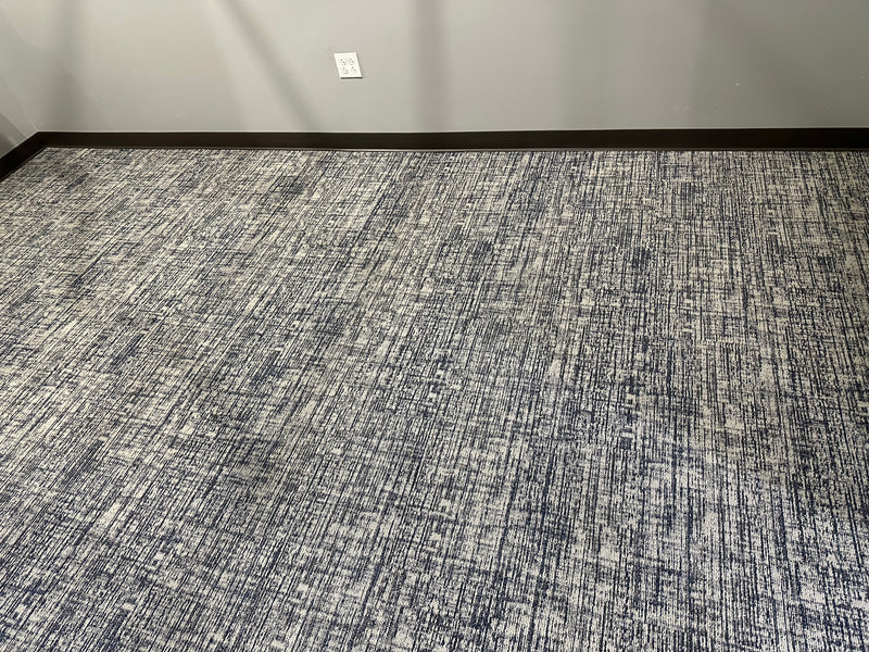 Textured gray carpet in a room with a light-colored wall and black baseboard.