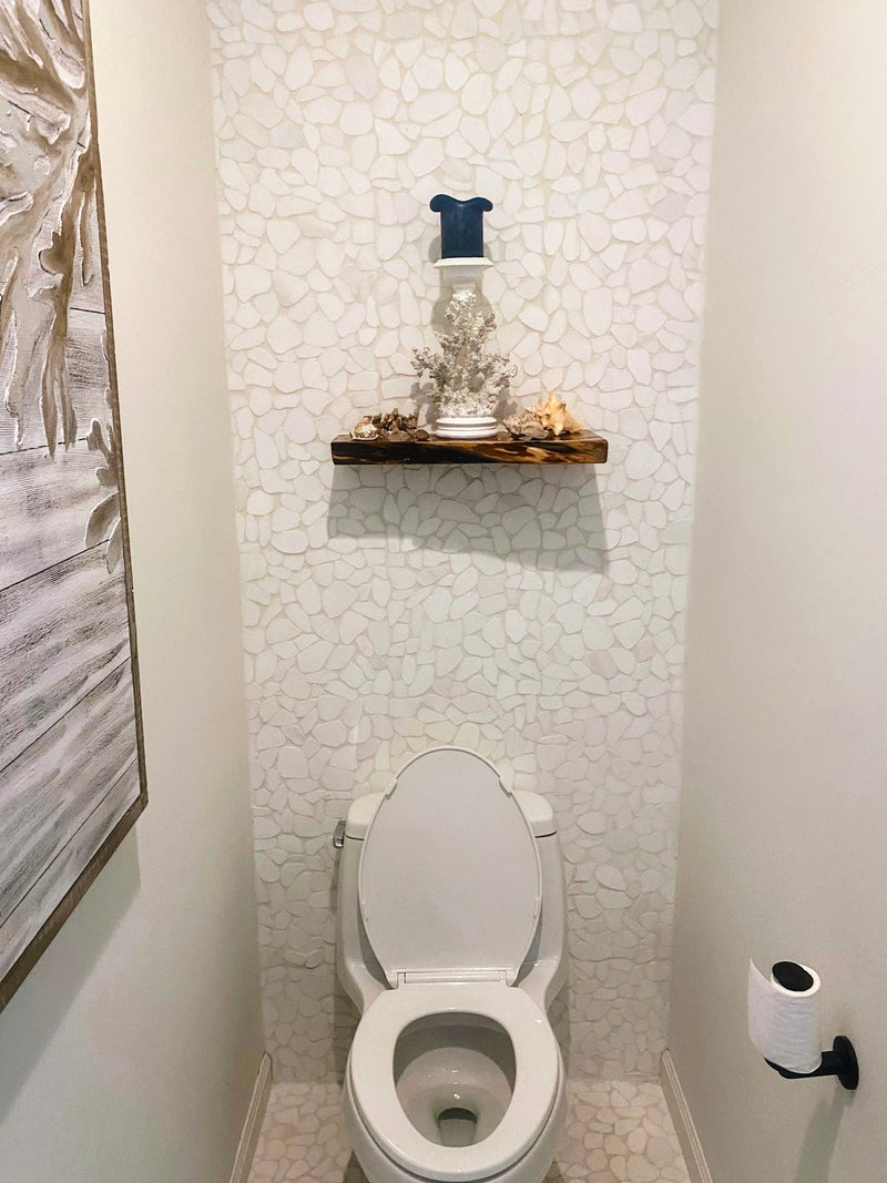 Small bathroom with white toilet, mosaic tile wall, and wooden shelf.