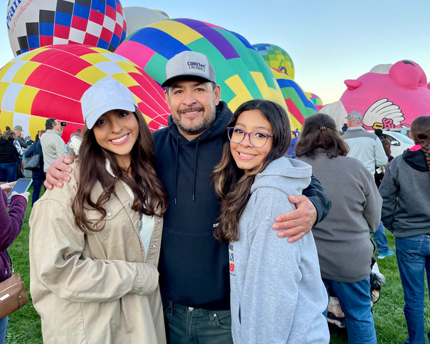 Three people posing in front of colorful hot air balloons at a festival.