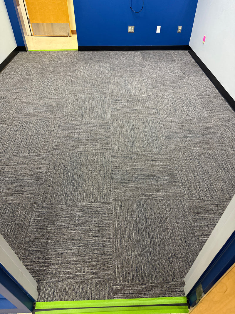 Gray carpeted floor in a room with blue walls and a yellow door.